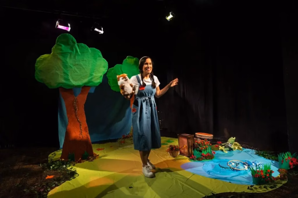 Plano general de la escenografía de La ardilla Lula con árboles, lago y Paloma Mariscal sosteniendo el títere de la ardilla
